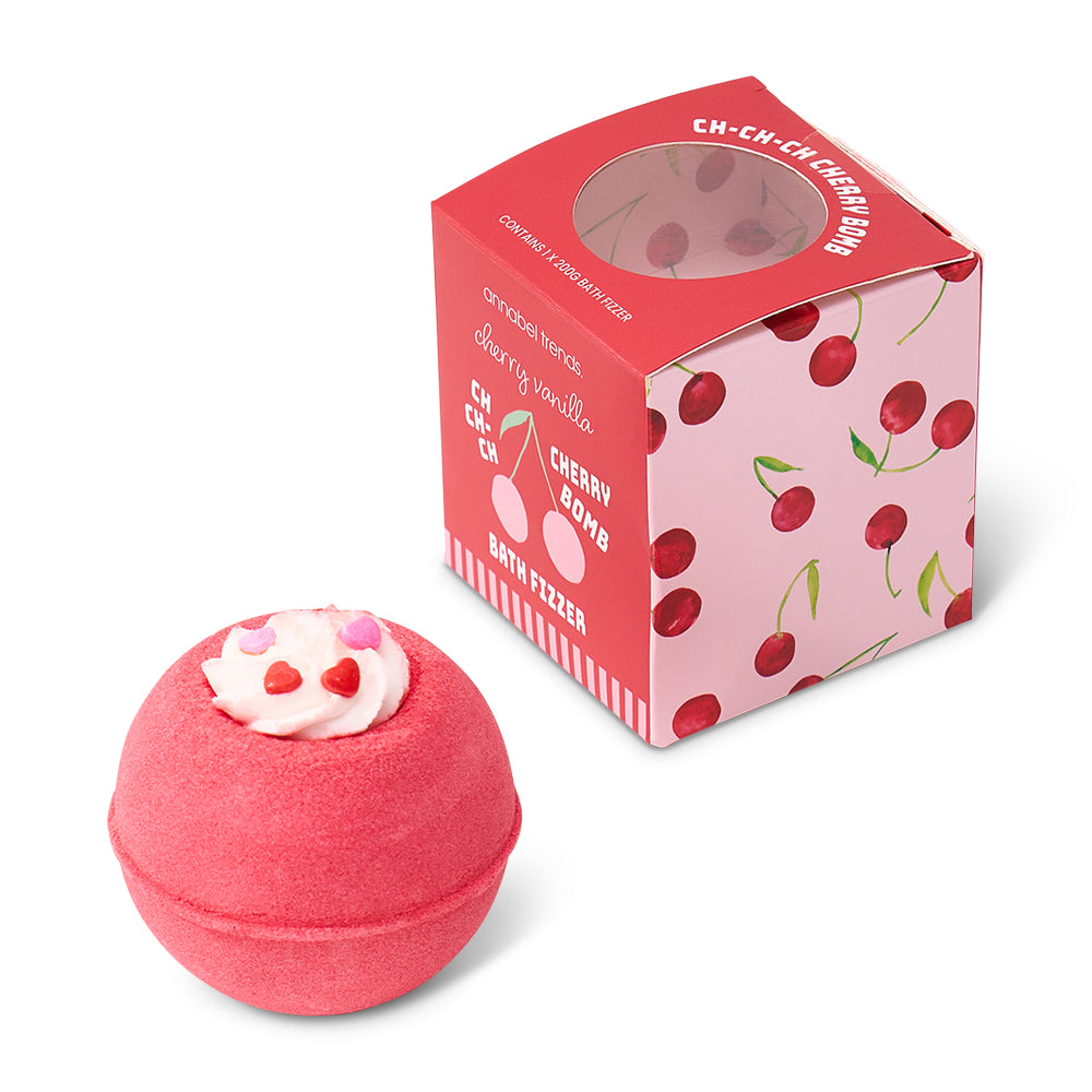 Pink bath bomb with cherry design next to its packaging on a white background