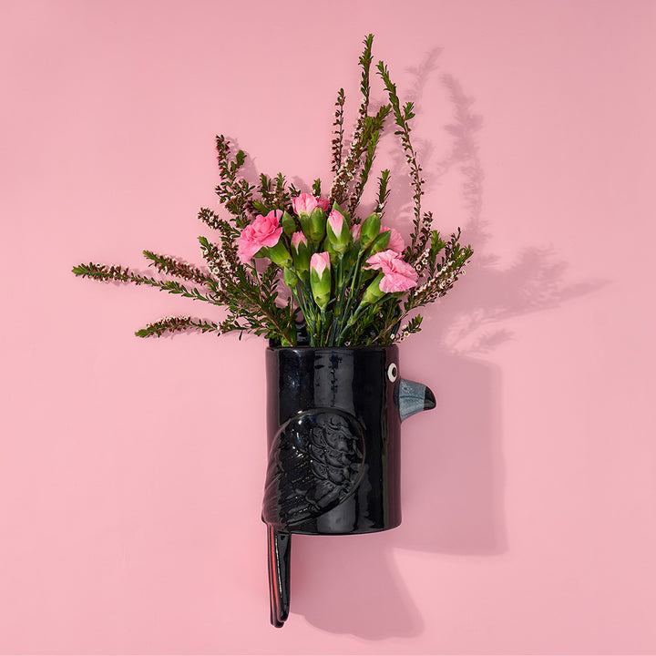 Black vase shaped like a black cockatoo with pink flowers on a pink background