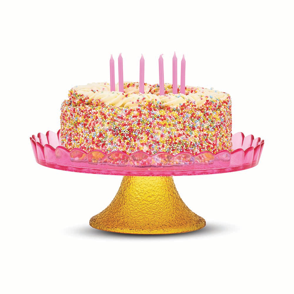 Colorful birthday cake with pink candles on a pink and yellow cake stand against a white background