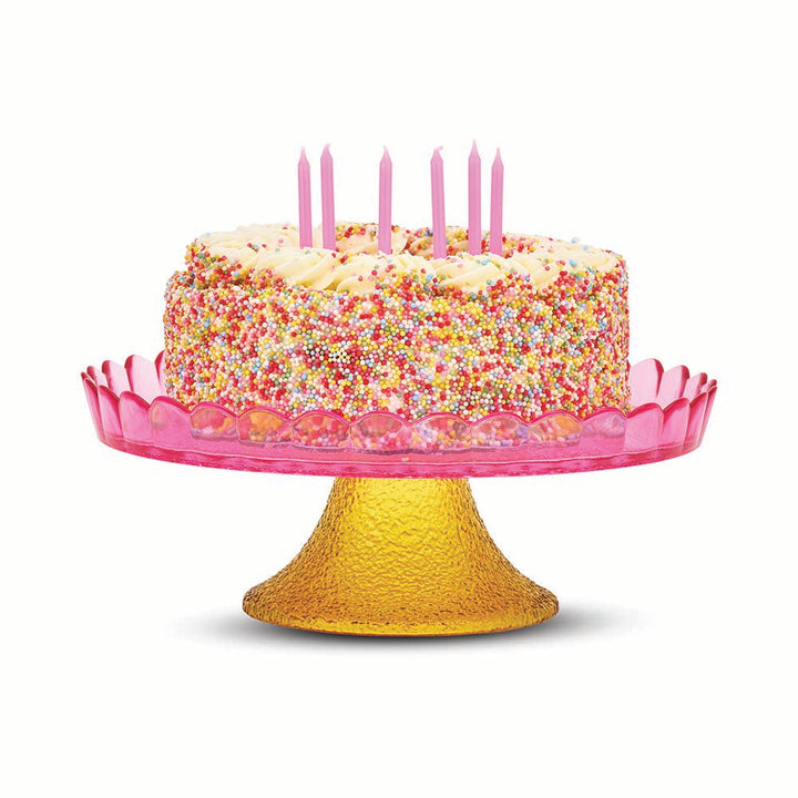 Colorful birthday cake with pink candles on a pink and yellow cake stand against a white background