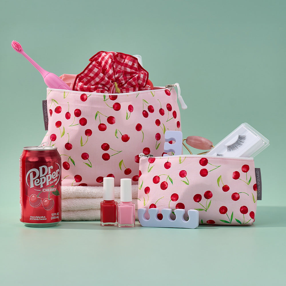 Pink toiletry bag with cherry pattern, nail polish, and a can of Dr Pepper on a light green background