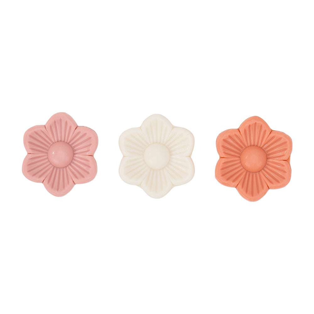Three floral-shaped soaps in pink, white, and coral on a white background