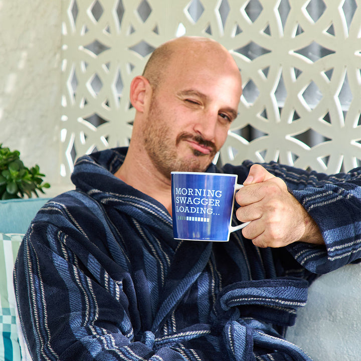 Man in a robe holding a mug with 'Morning Swagger Loading' text, sitting on a chair.