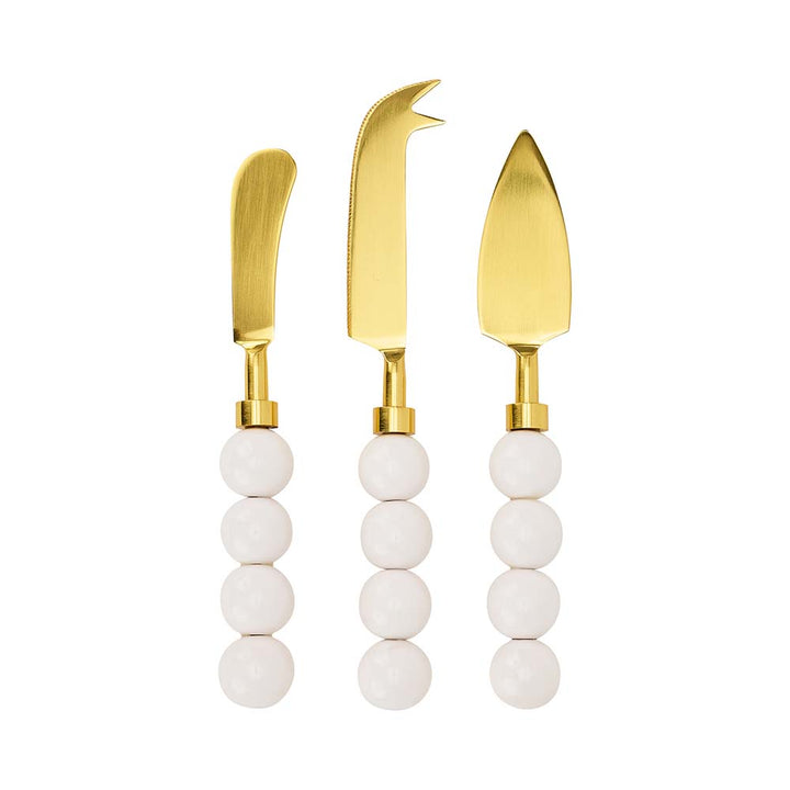 Three gold cheese knives with white bead handles on a white background