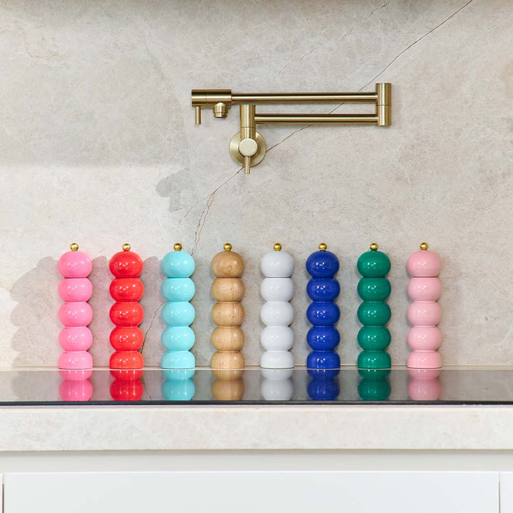Colorful cylindrical Salt and Pepper mills on a reflective surface with a gold faucet in the background.