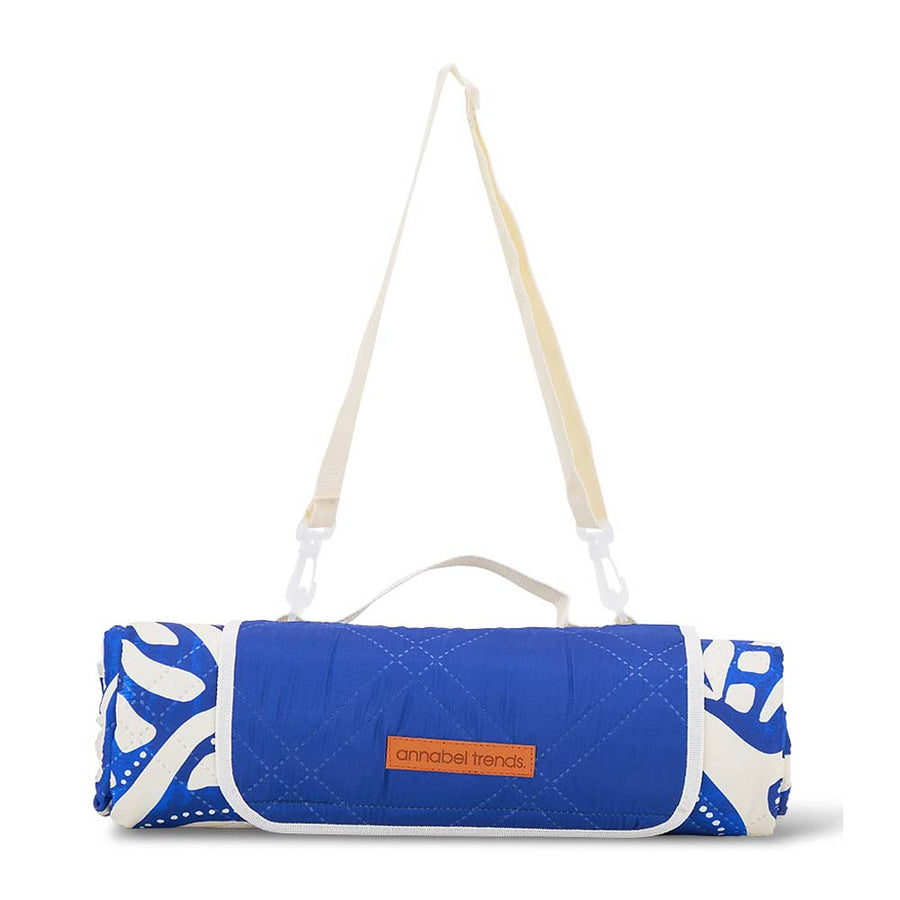 Blue and white patterned picnic mat rolled up with a strap on a white background