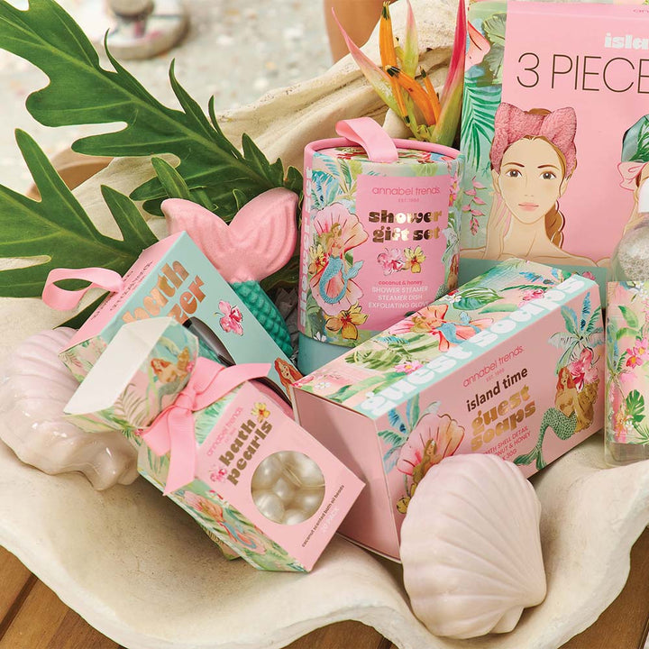 Assorted beauty products including soaps and bath bombs on a shell with tropical leaves.