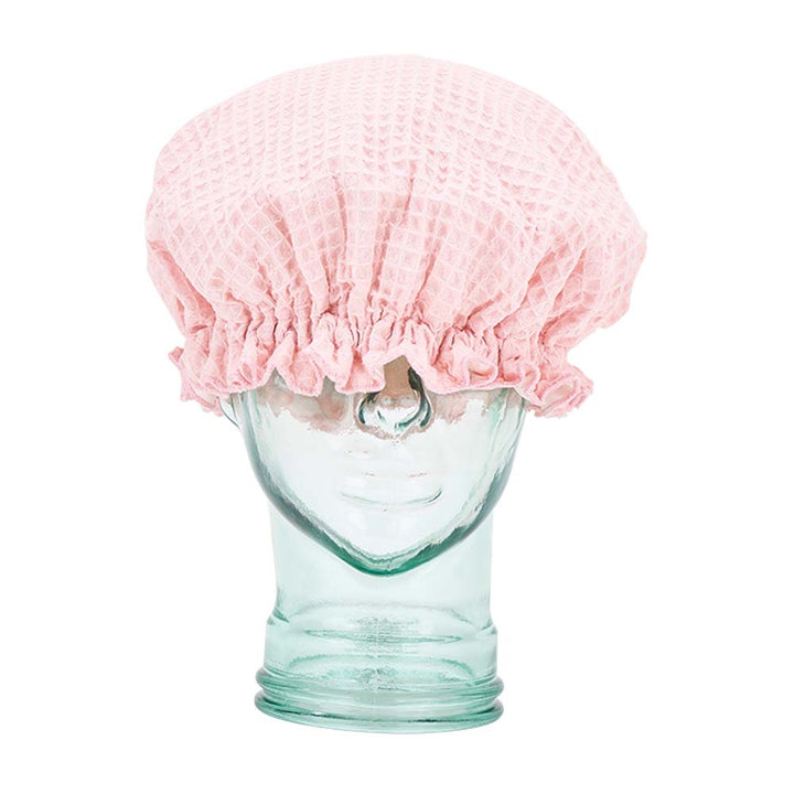 Clear glass mannequin head with a pink textured shower cap on a white background