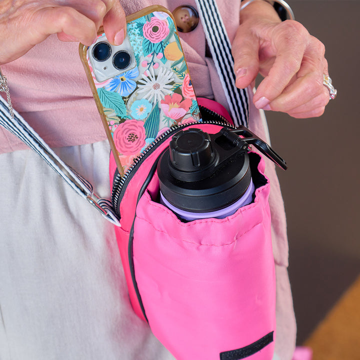 Person holding a pink crossbody bottle bag with a phone and black water bottle.