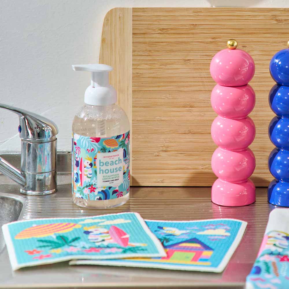 Hand soap bottle with beach-themed packaging on a kitchen counter next to colorful towels and salt and pepper shakers.