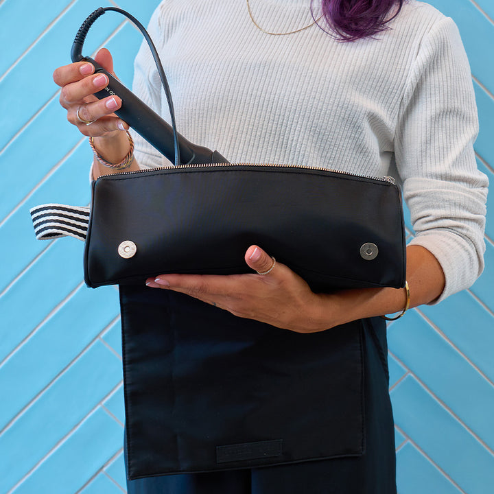 Person holding a black hair straightener bag against a blue tiled wall