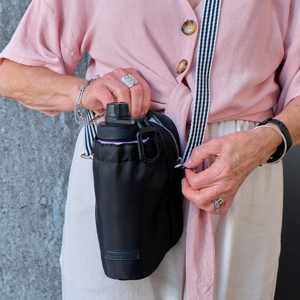 Person holding a black water bottle bag with a pink jacket and light pants.