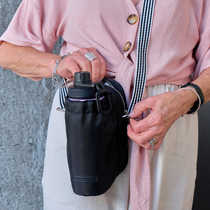 Person holding a black water bottle bag with a pink jacket and light pants.