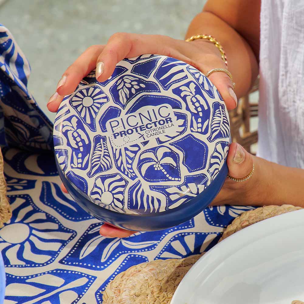 Person holding a blue and white patterned container labeled 'Picnic Protector' on a textured surface.