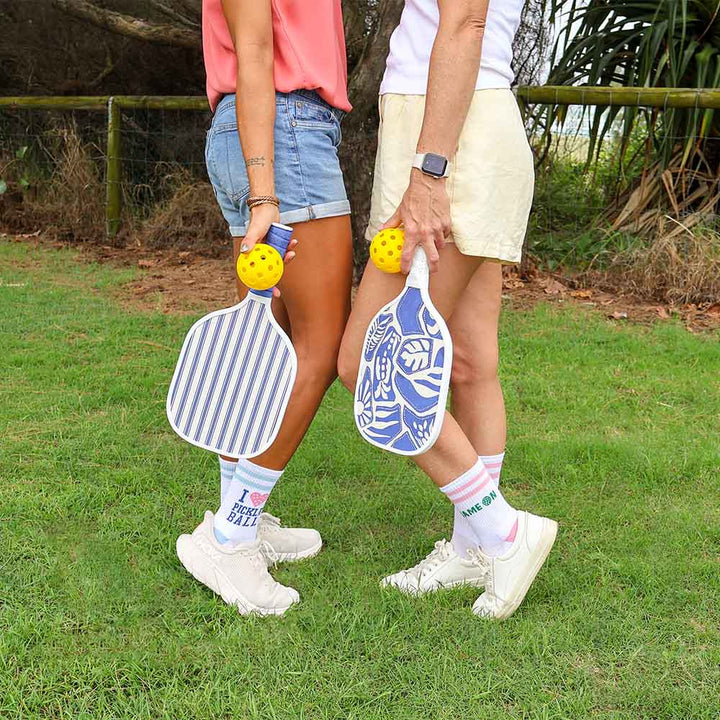 Two people holding pickleball paddles with yellow balls on a grassy field.