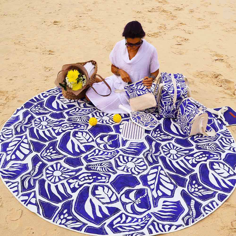 Person sitting on a large blue and white patterned beach towel on a sandy beach.