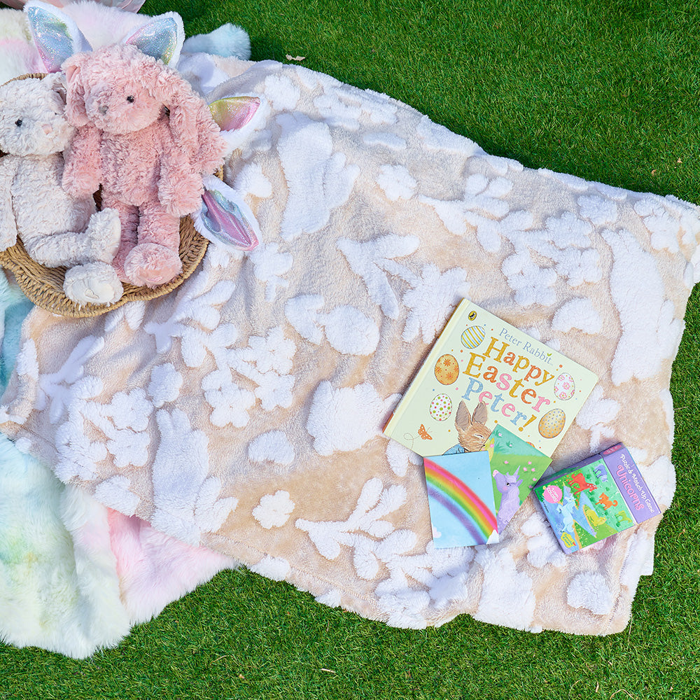 Floral-bunny-patterned blanket with plush toys and children's books on a grassy background