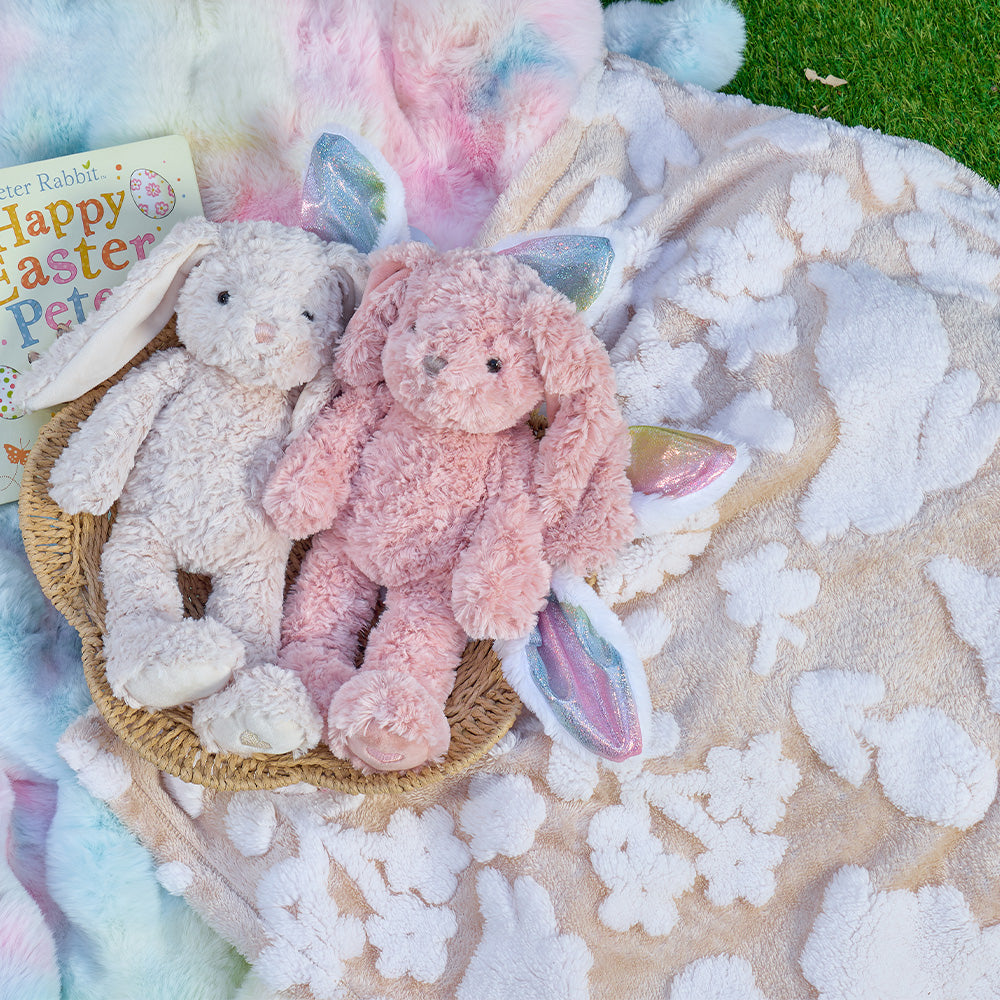 Two plush bunny toys in a basket on a floral blanket with Easter decorations.