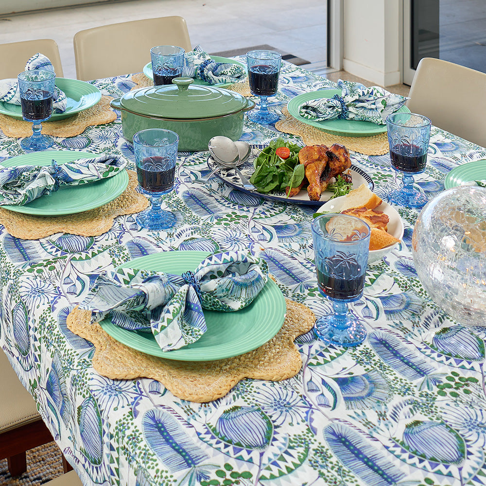 Dining table set with a patterned tablecloth, green plates, blue glasses, and food.