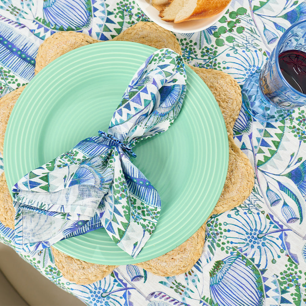 Green plate with a blue and white patterned napkin on a colorful tablecloth.