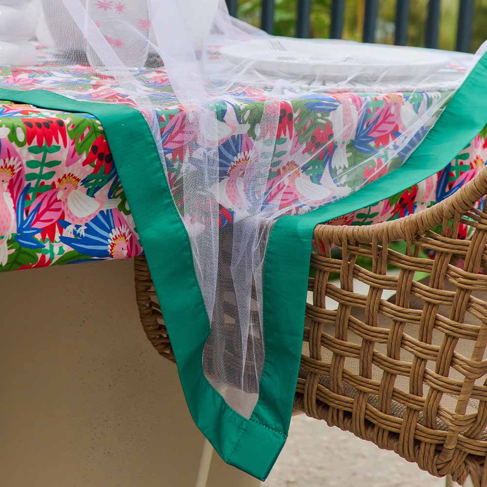 Colorful floral tablecloth with green trim draped over a wicker chair outdoors with buzz off fly netting draped over table