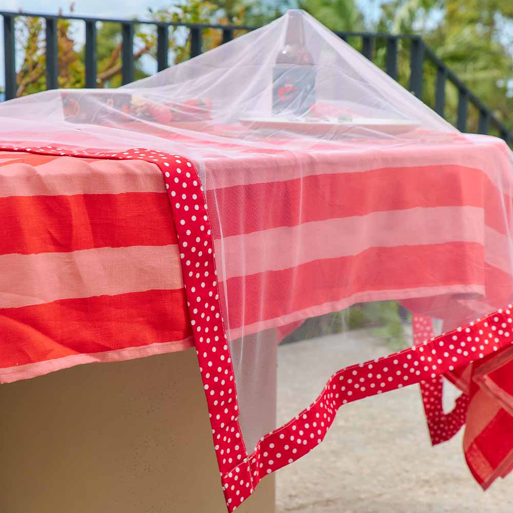 Red and white striped tablecloth with a polka dot border on a table outdoors.