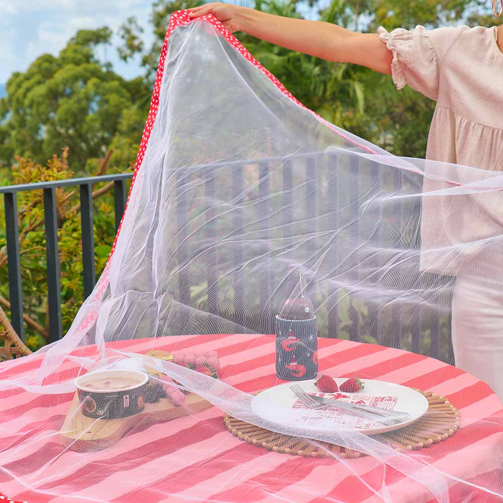 Person setting up a mosquito net over a table with food and drinks on a balcony.