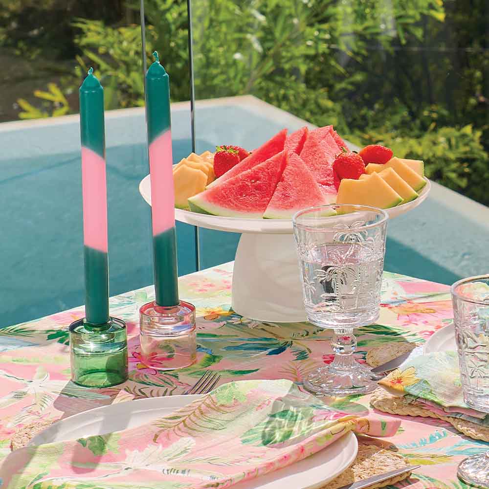 Outdoor table setting with watermelon, melon, and candles on a floral tablecloth.