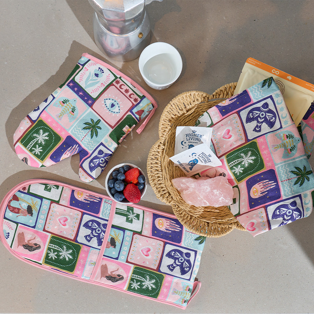 Colorful oven mitts and tea towel with geometric celestial dreams pattern on a table with berries and a crystal.