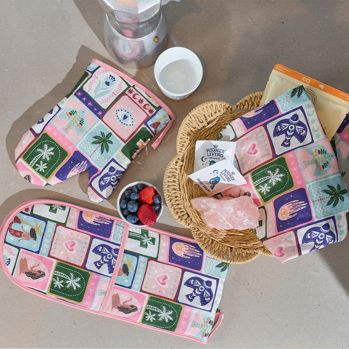 Colorful oven mitts and tea towel with geometric celestial dreams pattern on a table with berries and a crystal.