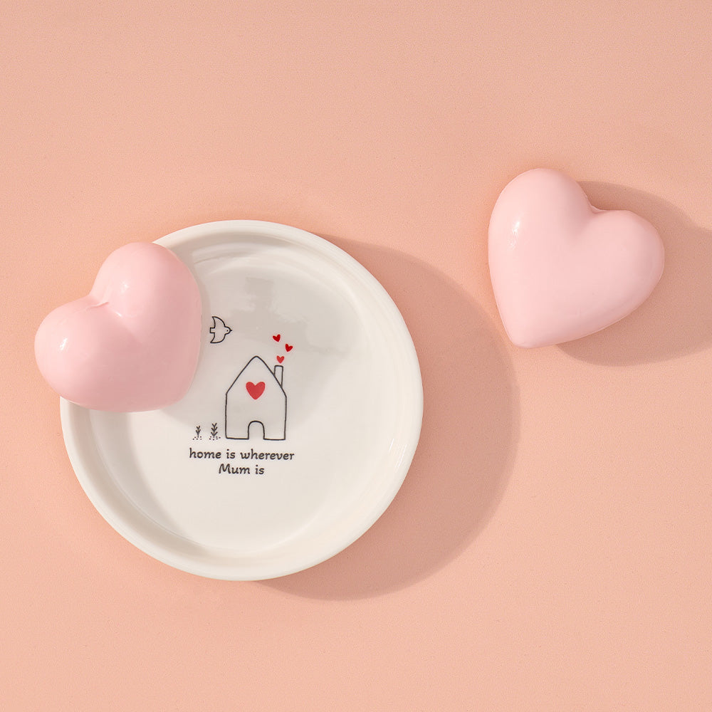 White dish with heart design and text, surrounded by pink hearts on a peach background