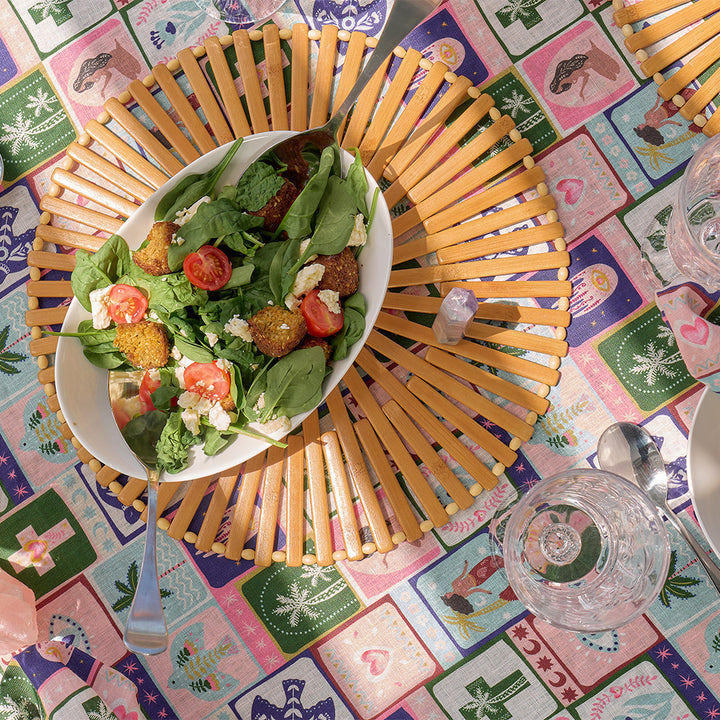 Salad in a white bowl on a wooden placemat with a colorful tablecloth underneath with celestial dreams design print