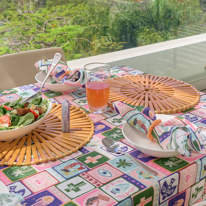 Outdoor dining table setting with a colorful tablecloth, salad, glass of juice, and decorative plates.