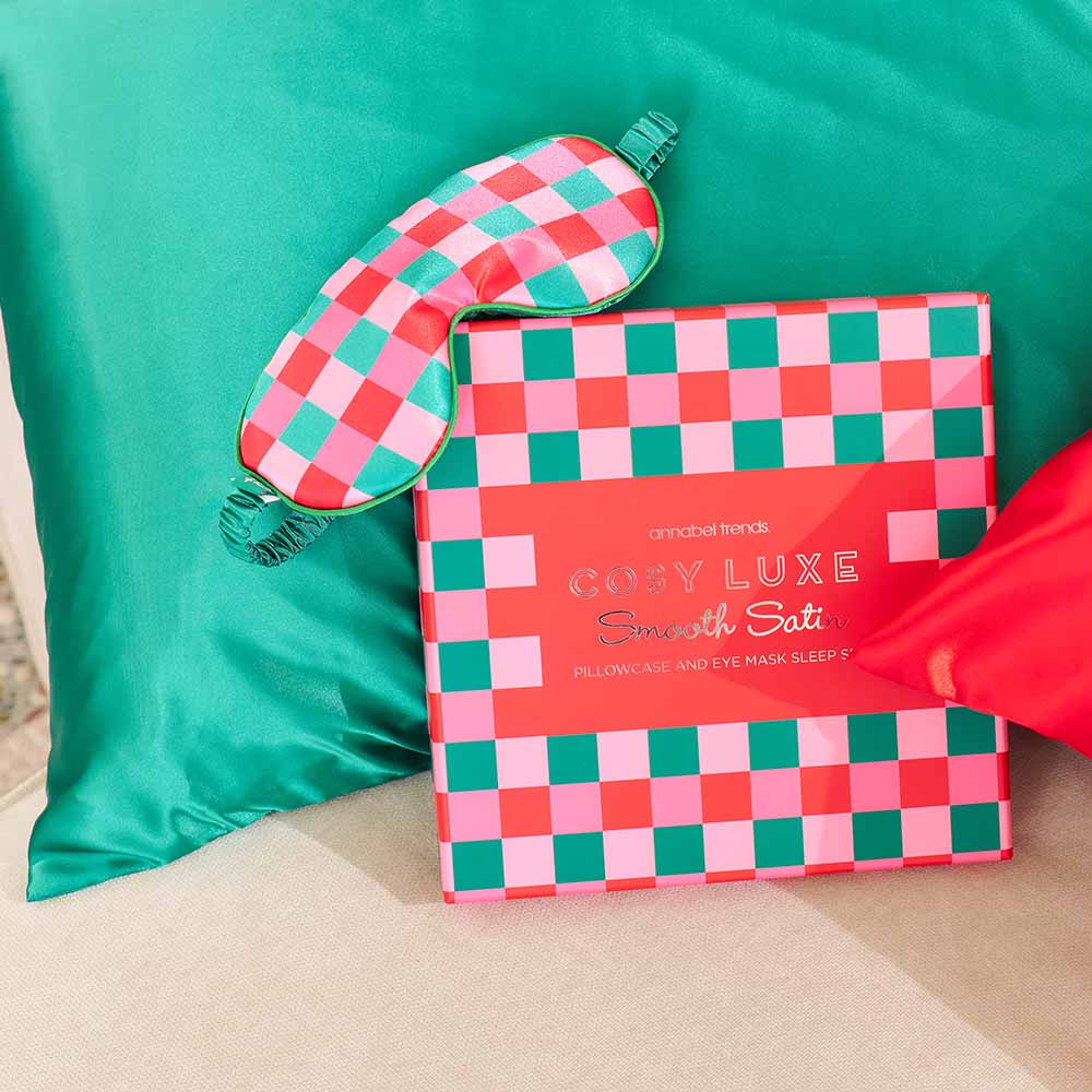 Checkered pillowcase and eye mask set on a green pillow with a red bow.