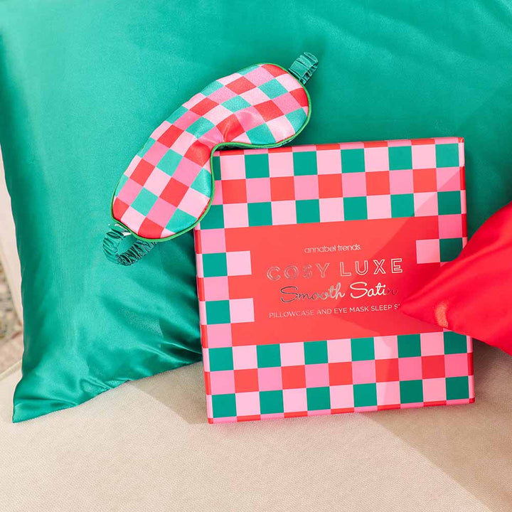 Checkered pillowcase and eye mask set on a green pillow with a red bow.