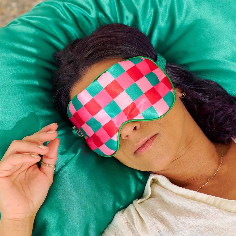 Person wearing a red and green checkered eye mask on a green pillow