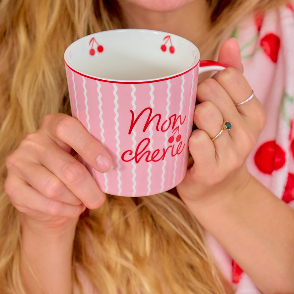 Person holding a pink mug with 'Mon Cherie' text and cherry design.