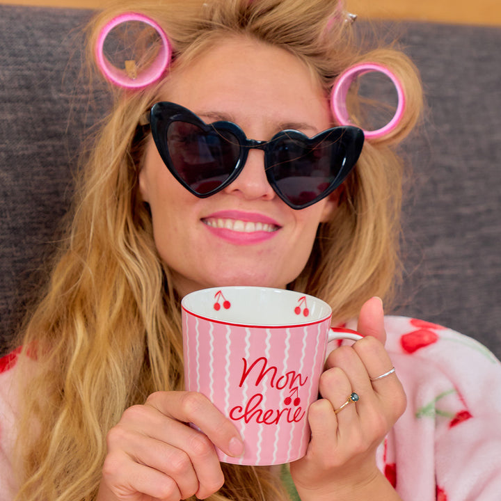 Woman with heart-shaped sunglasses and pink hair rollers holding a 'Mon Cherie' mug.