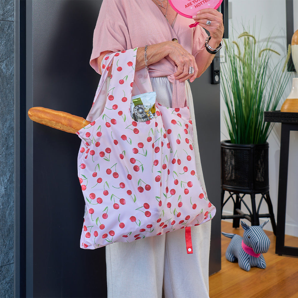 Person holding a cherry-patterned bag with a plant and small dog in the background