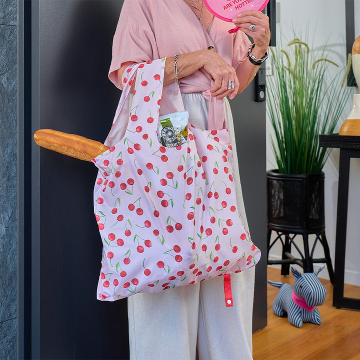 Person holding a cherry-patterned bag with a plant and small dog in the background