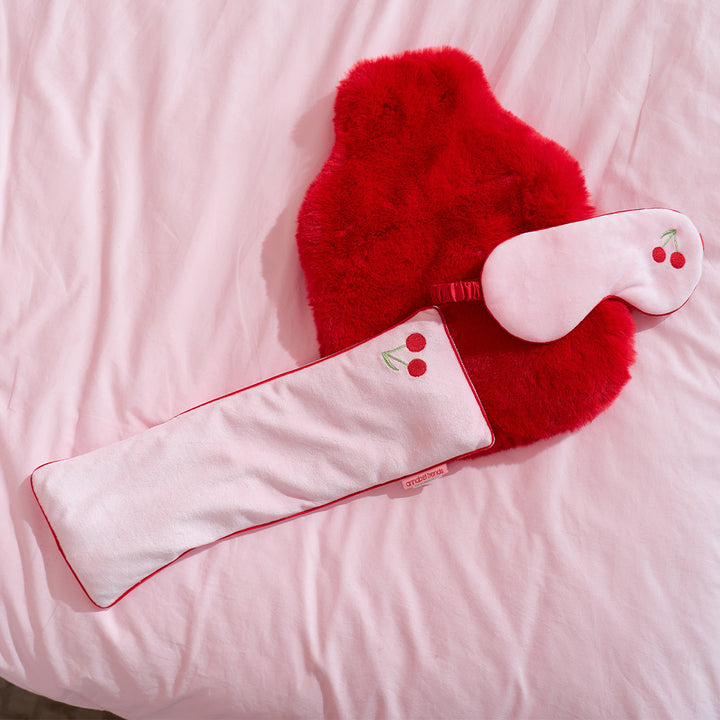 Red fuzzy eye mask and pillow with cherry design on a pink background