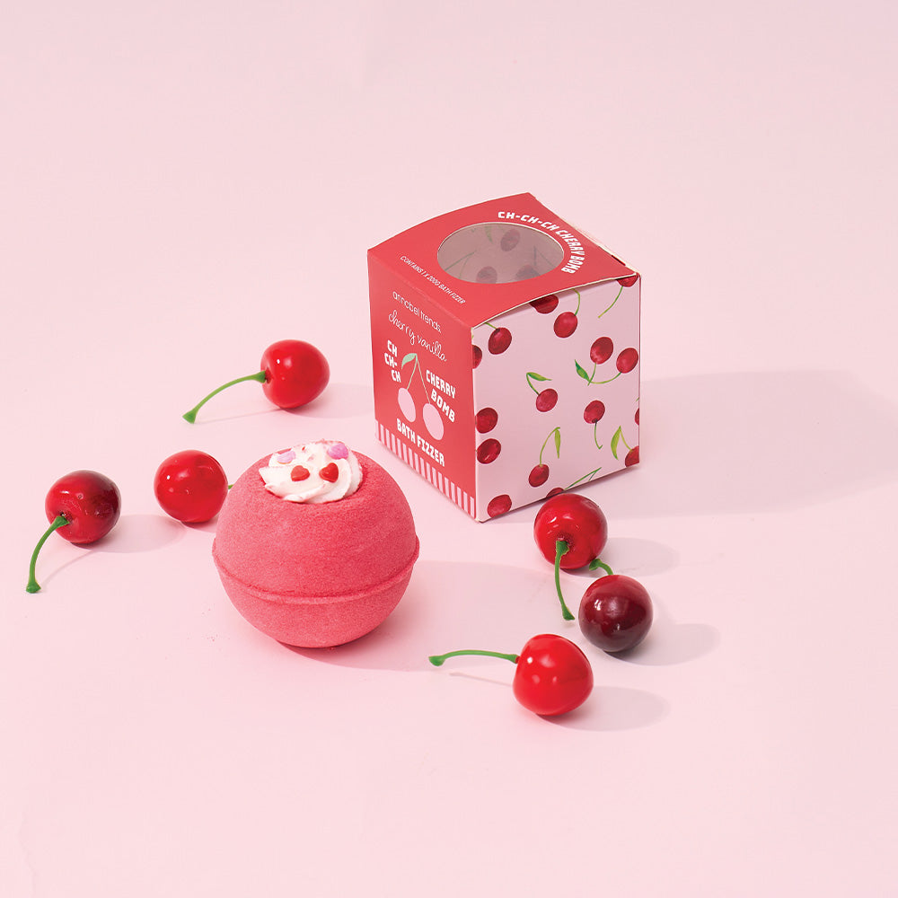 Pink cherry-themed bath bomb with packaging on a pink background