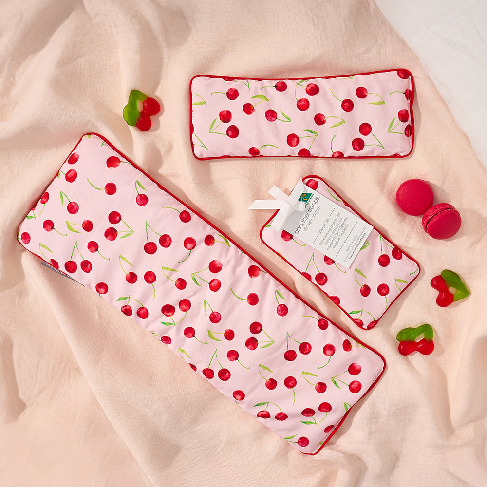 Set of pink heat pillows, eye rest pillow and drawer sachet with cherry pattern on a beige surface