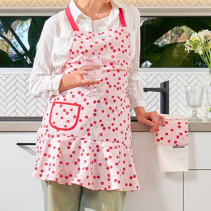 Person wearing a pink apron with red cherry design in a kitchen.
