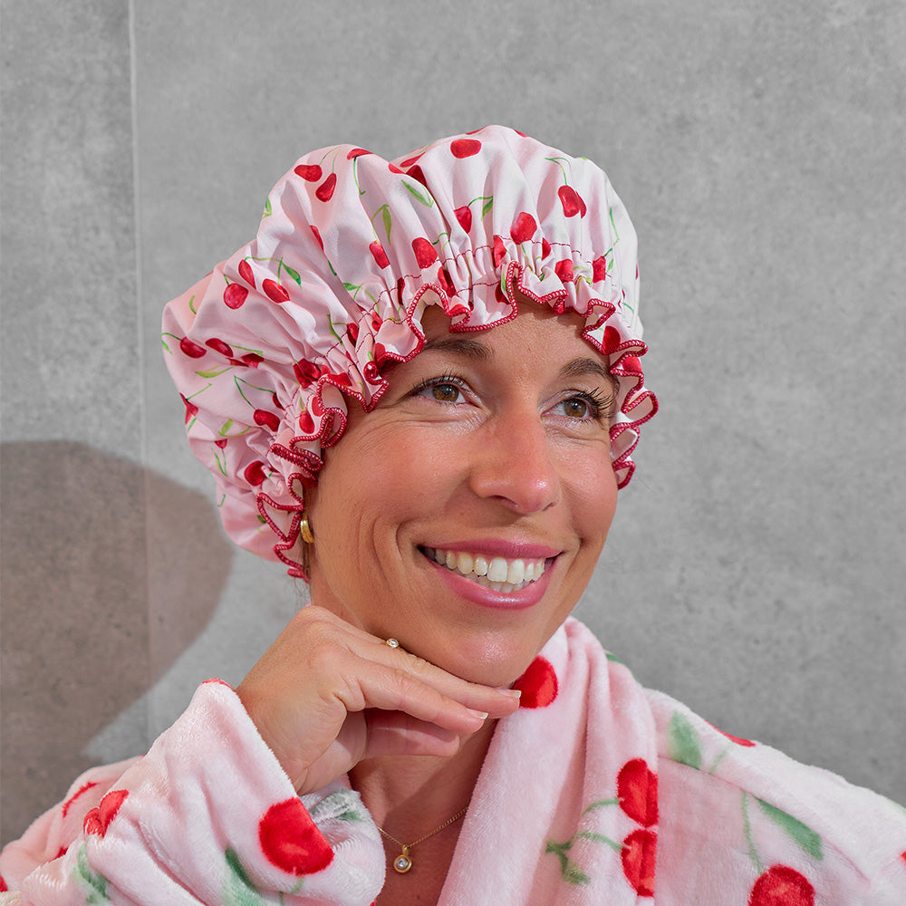 Woman wearing a pink shower cap with cherry pattern in a bathroom setting