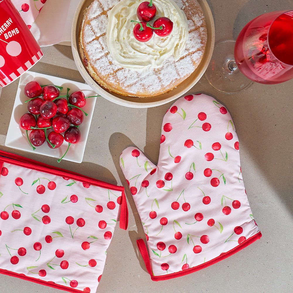 Cherry-themed kitchen items including a cake, oven mitt, and pot holder on a table.