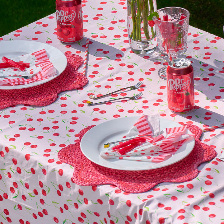 Outdoor table setting with Dr Pepper cans, plates, and cutlery on a cherry-themed tablecloth.