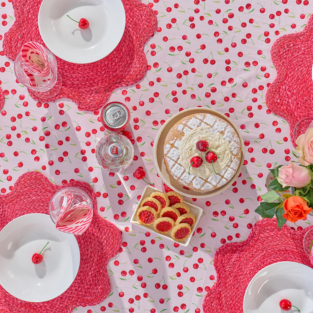 Table setting with a cake, pastries, and drinks on a polka dot tablecloth with red cherries.