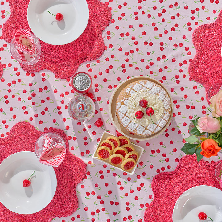 Table setting with a cake, pastries, and drinks on a polka dot tablecloth with red cherries.