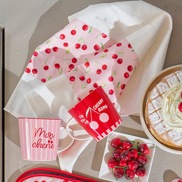 Cherry-themed kitchen items including a mug, napkins, and a cake on a neutral background